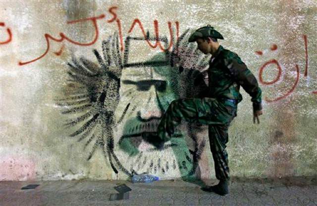 A rebel fighter kicks graffiti of Gadhafi.